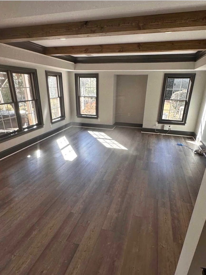 Finished residential interior with stained ceiling beams, black-trimmed windows and wide dark plank flooring run wall to wall.