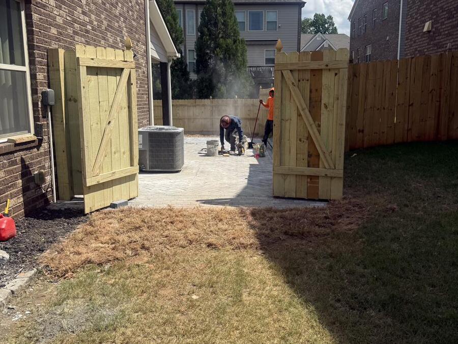 Before: a patchy side-yard lawn beside a new fence, with paver setting underway on the far end.