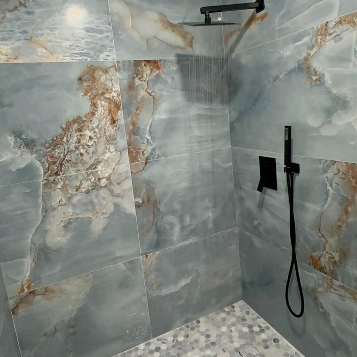 Walk-in shower lined in blue onyx-look panels, with a hexagonal marble mosaic floor and a linear drain.
