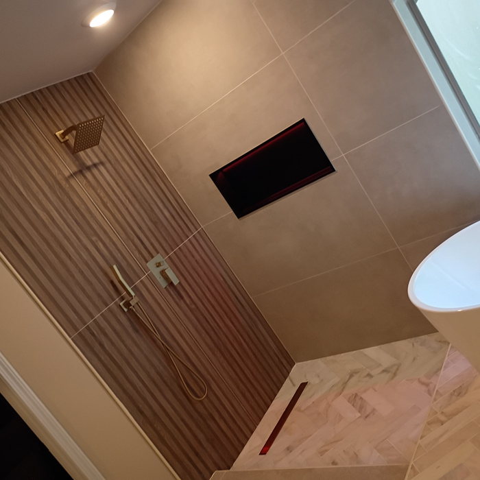 Walk-in shower with a fluted wood-look tile wall, brushed gold rain head and handset, a recessed lit niche and a herringbone marble floor with a linear drain.
