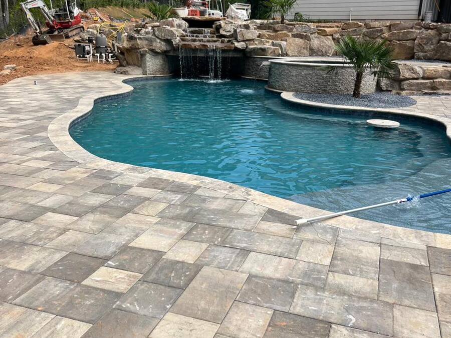 Freeform pool with stone waterfall and a large-format travertine paver deck.