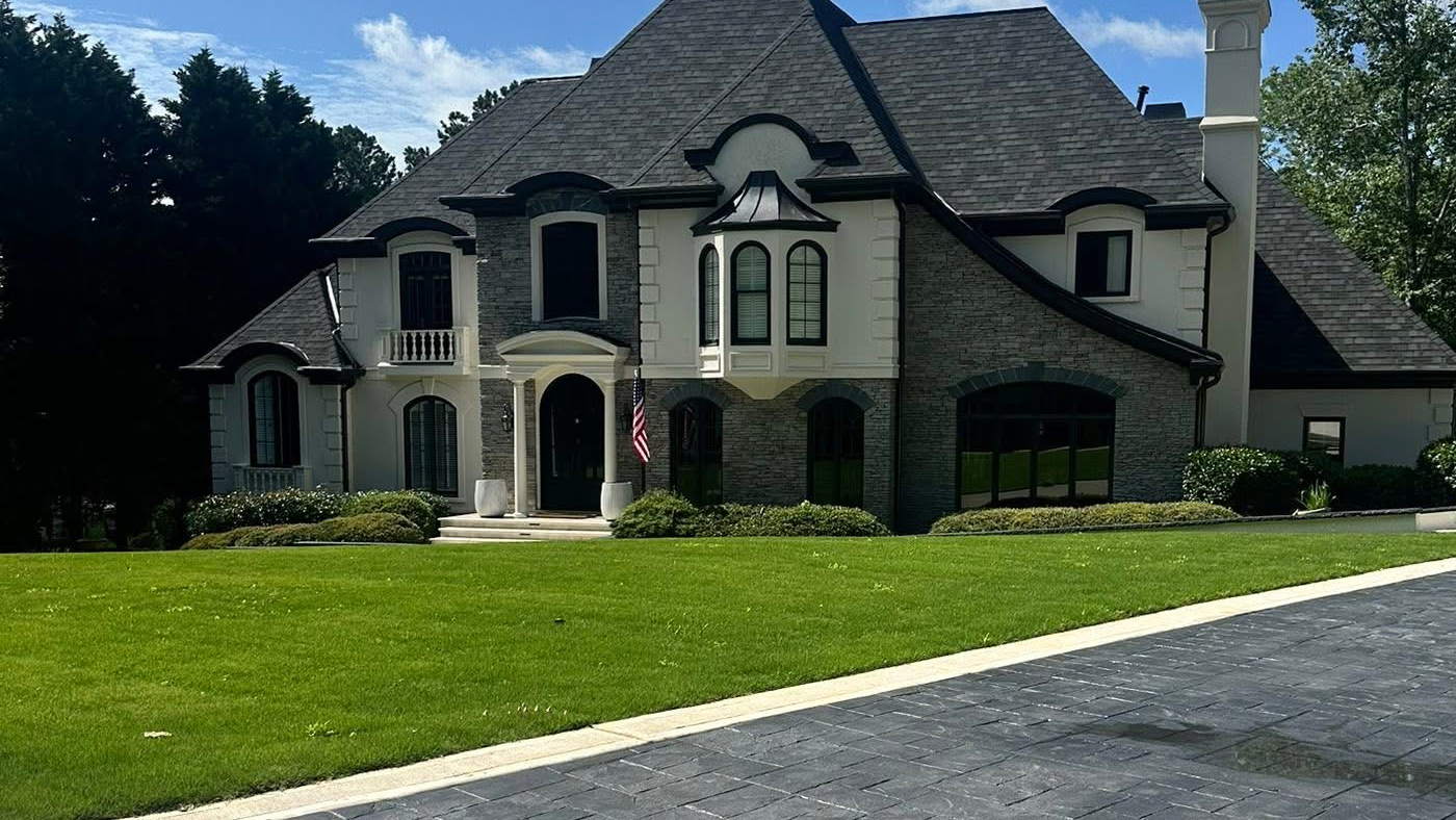 Stamped slate-pattern concrete driveway sweeping past a manicured lawn to a large stone and stucco home.