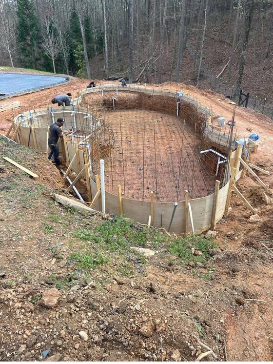 Steel reinforcement grid tied inside a formed pool excavation, with crew working the perimeter.