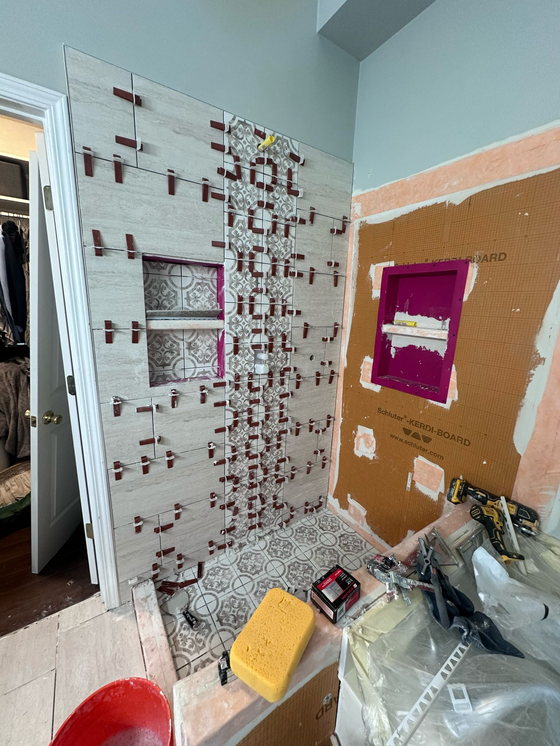 Shower wall part-tiled over an orange waterproofing board, with a bonded niche pan and tile leveling clips still in place.