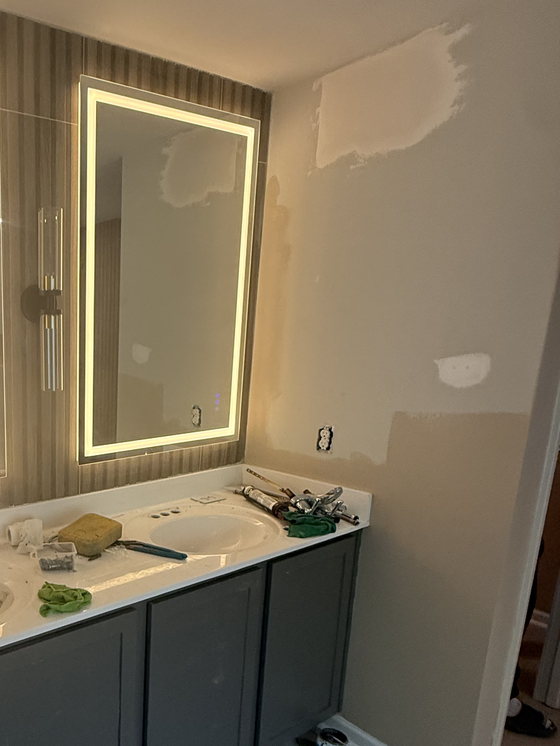 Vanity being installed, with a backlit mirror already lit above the counter and tap fittings laid out ready to set.