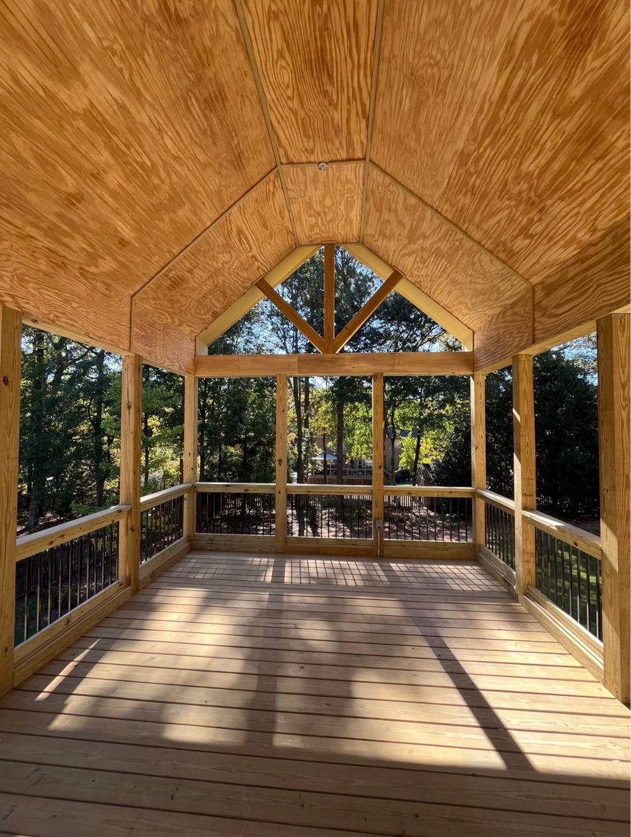 Inside the finished covered deck, looking out through the gable end to the woods, under a vaulted timber ceiling.
