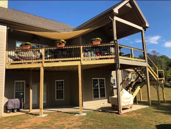 Finished outdoor living: a two-level deck in use, with dining furniture, planters, a shade sail and string lighting.