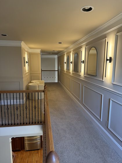 After: the finished hallway with panelled wainscot, arched mirrors and vertical sconces.