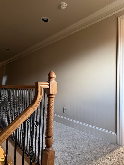 Before: bare landing wall in flat paint above carpet, beside the original oak stair railing.