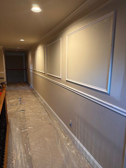 In progress: panel moulding and chair rail set and primed along the hallway, with floors covered in protective sheeting.
