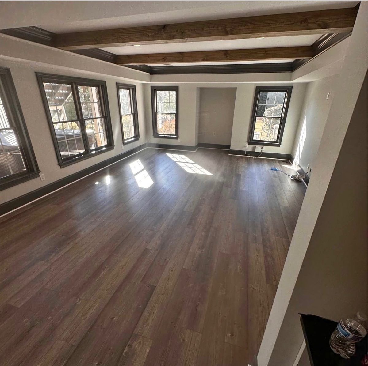 Finished living room with stained ceiling beams, black window trim and wide dark plank flooring.
