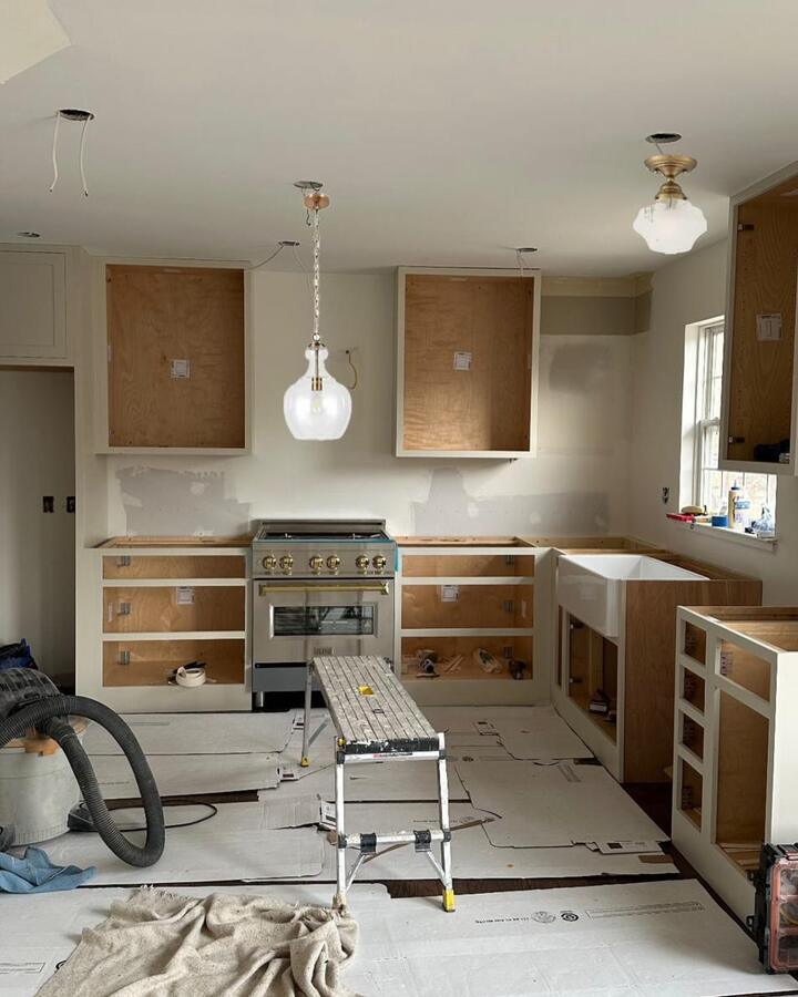 Kitchen mid-installation with base cabinets set, a range in place, farmhouse sink and glass pendant lights hung.